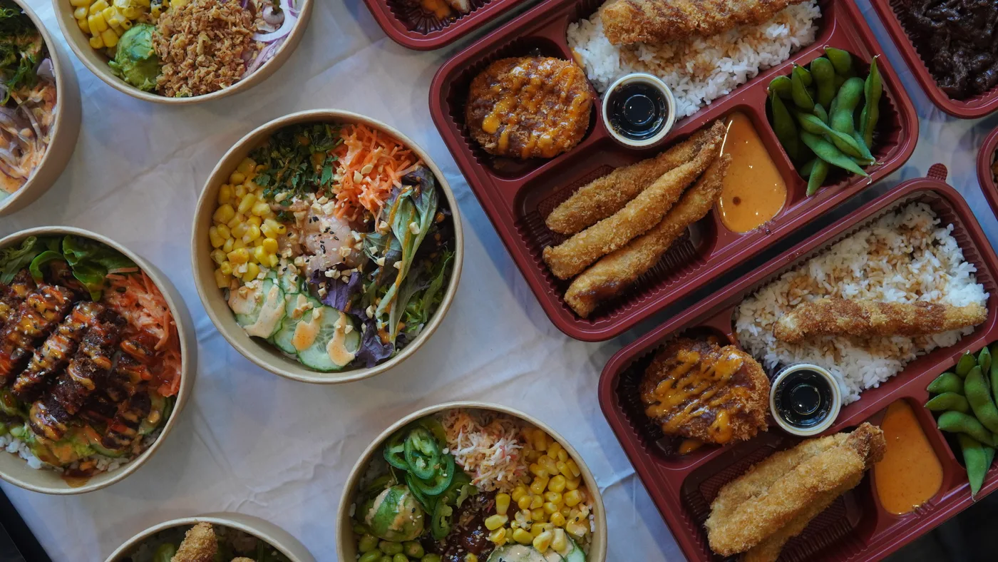 Bowls and bento trays with breaded shrimp, edamame and rice, seen from above